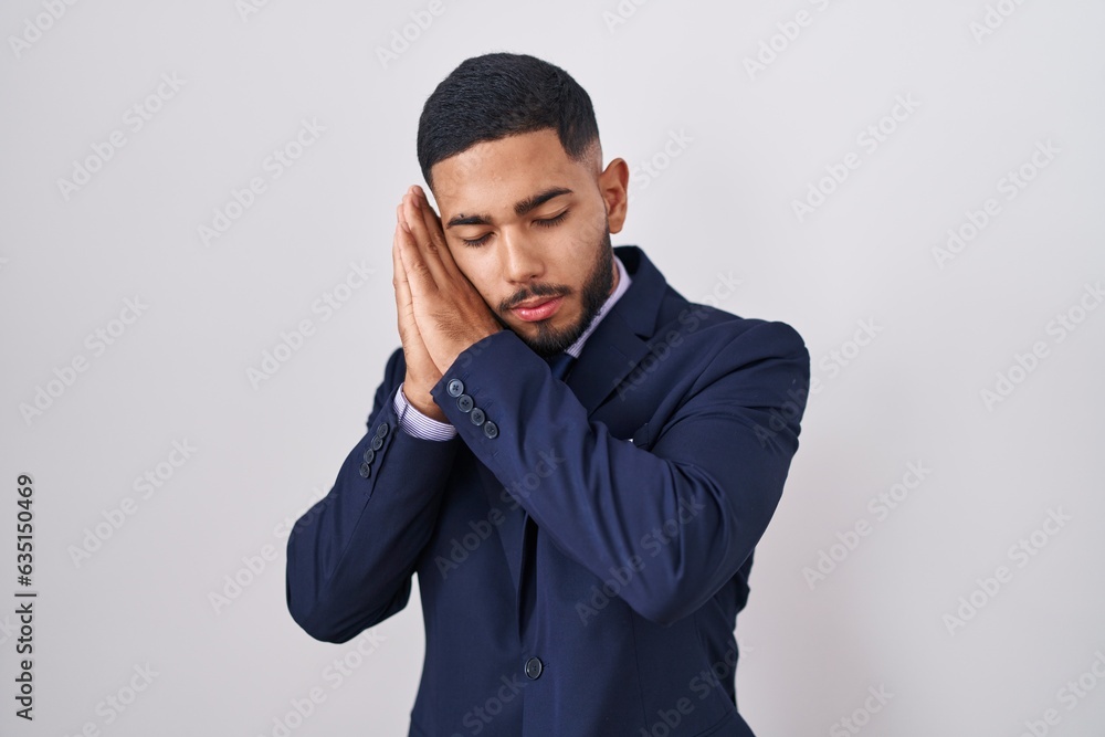 Young hispanic man wearing business suit and tie sleeping tired dreaming and posing with hands together while smiling with closed eyes. Young hispanic man wearing business suit and tie sleeping tired dreaming and posing with hands together while smiling with closed eyes.