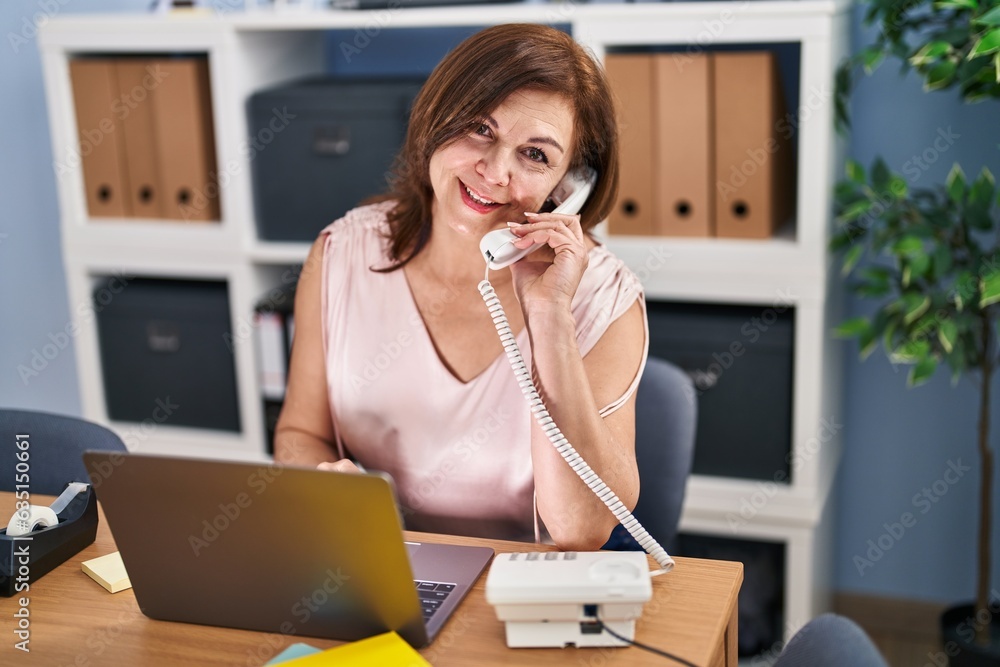 Middle age woman business worker talking on telephone using laptop at office Middle age woman business worker talking on telephone using laptop at office
