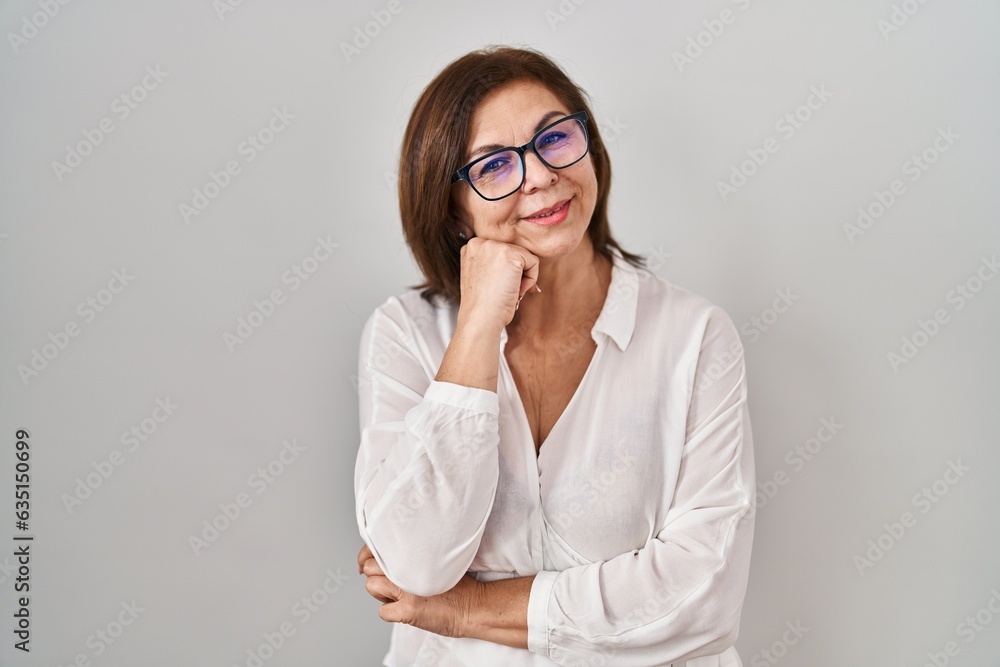 Middle age hispanic woman standing over isolated background with hand on chin thinking about question, pensive expression. smiling with thoughtful face. doubt concept. Middle age hispanic woman standing over isolated background with hand on chin thinking about question, pensive expression. smiling with thoughtful face. doubt concept.