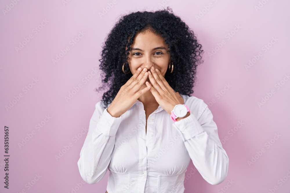 Hispanic woman with curly hair standing over pink background laughing and embarrassed giggle covering mouth with hands, gossip and scandal concept Hispanic woman with curly hair standing over pink background laughing and embarrassed giggle covering mouth with hands, gossip and scandal concept