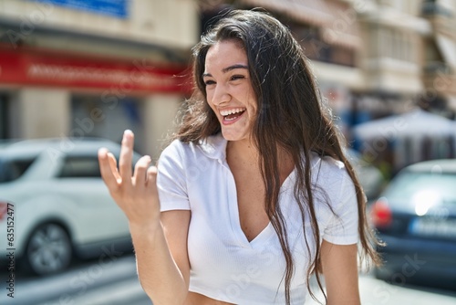 Young hispanic woman smiling confident doing coming gesture with hand at street