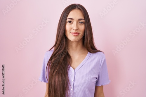 Young hispanic woman with long hair standing over pink background relaxed with serious expression on face. simple and natural looking at the camera.