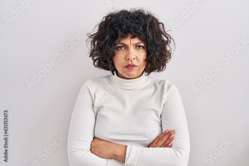 Hispanic woman with curly hair standing over isolated background skeptic and nervous, disapproving expression on face with crossed arms. negative person.