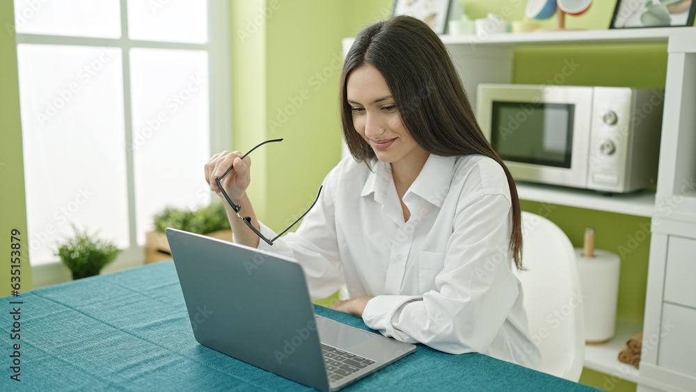 Young beautiful hispanic woman using laptop sitting on table at dinning room Young beautiful hispanic woman using laptop sitting on table at dinning room