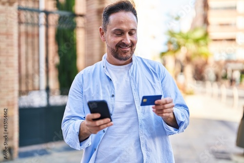Young caucasian man using smartphone and credit card at street