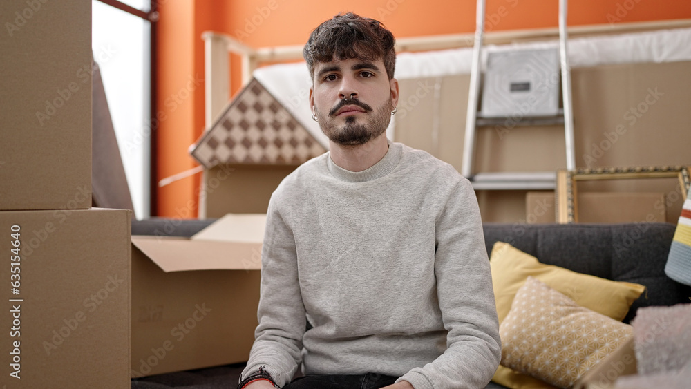Fototapeta premium Young hispanic man sitting on the sofa serious at new home