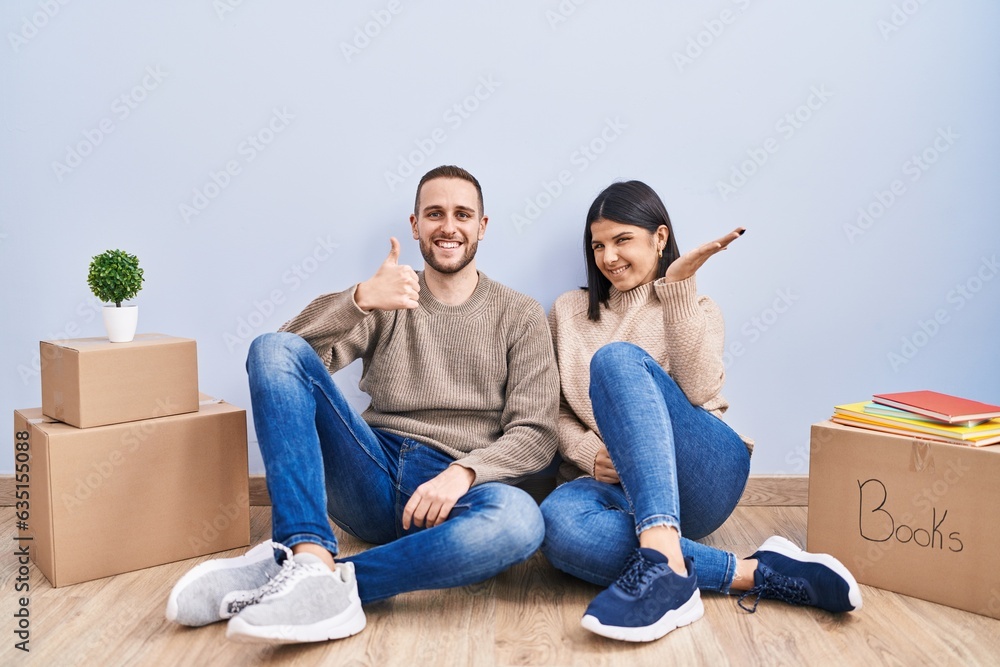 Young couple moving to a new home showing palm hand and doing ok gesture with thumbs up, smiling happy and cheerful Young couple moving to a new home showing palm hand and doing ok gesture with thumbs up, smiling happy and cheerful