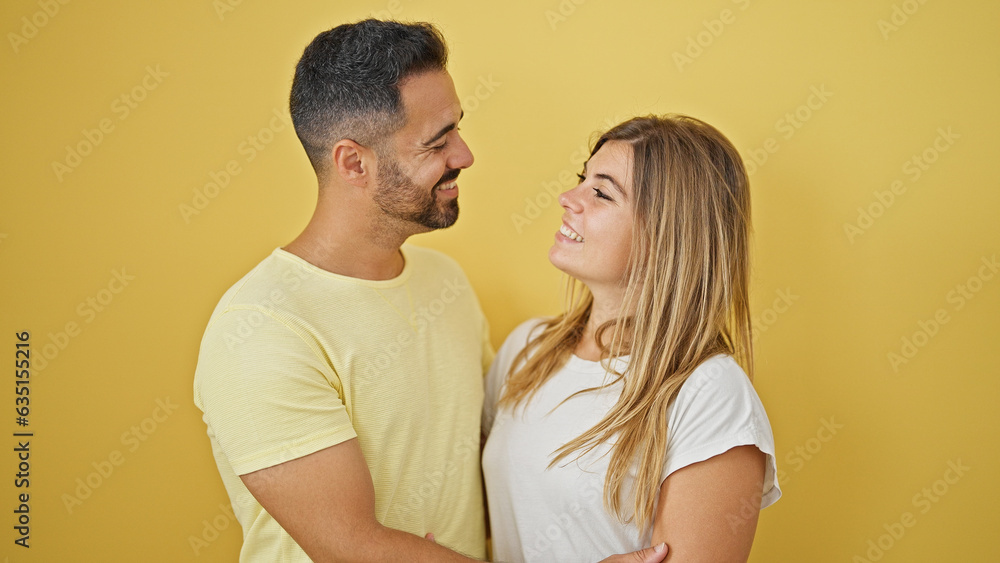Man and woman couple smiling confident hugging and looking each other over isolated yellow background Man and woman couple smiling confident hugging and looking each other over isolated yellow background