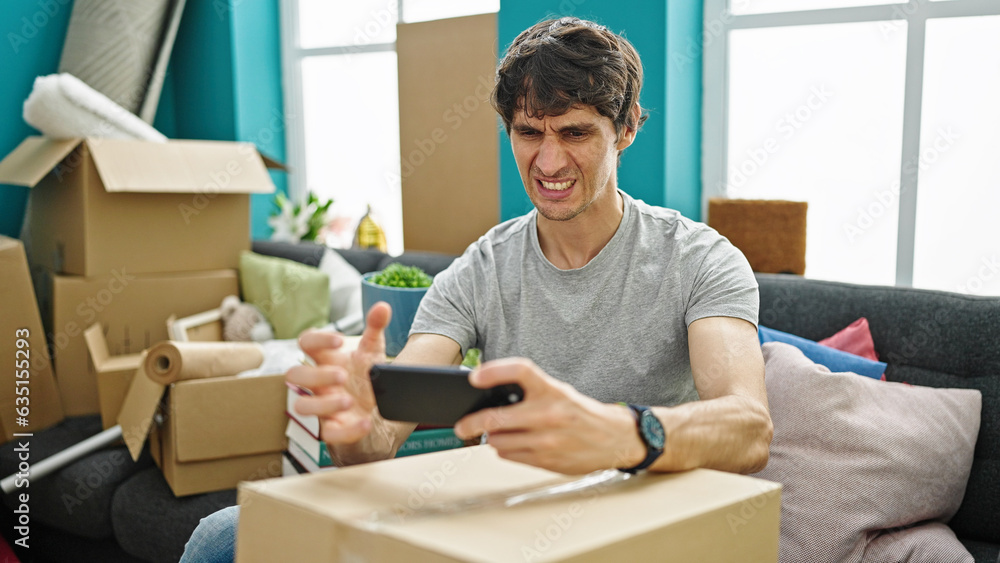 Young hispanic man playing video game looking upset at new home Young hispanic man playing video game looking upset at new home