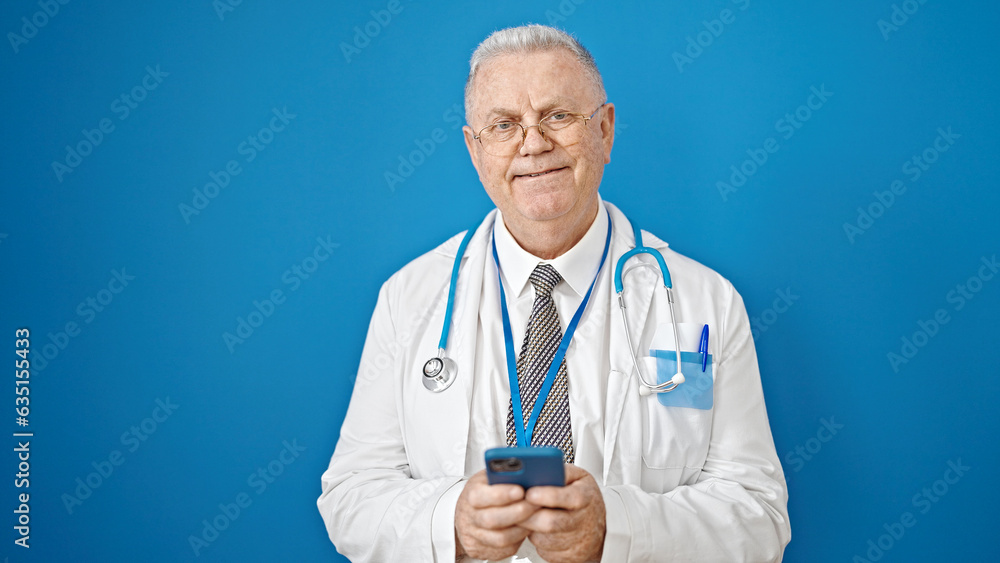 Middle age grey-haired man doctor smiling using smartphone over isolated blue background Middle age grey-haired man doctor smiling using smartphone over isolated blue background