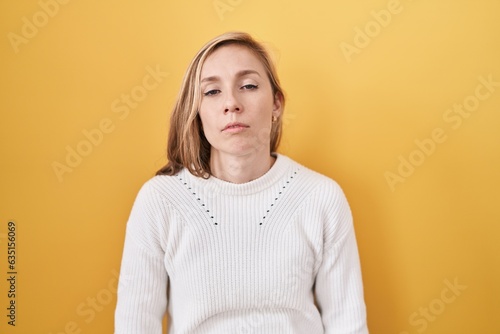Obraz na płótnie Young caucasian woman wearing white sweater over yellow background looking sleepy and tired, exhausted for fatigue and hangover, lazy eyes in the morning
