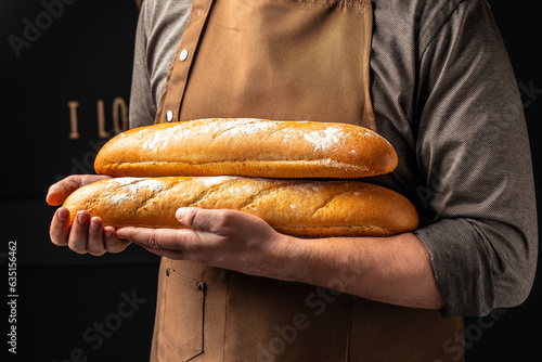 baguette in hand. bread in baker hands. bakery products on a dark background