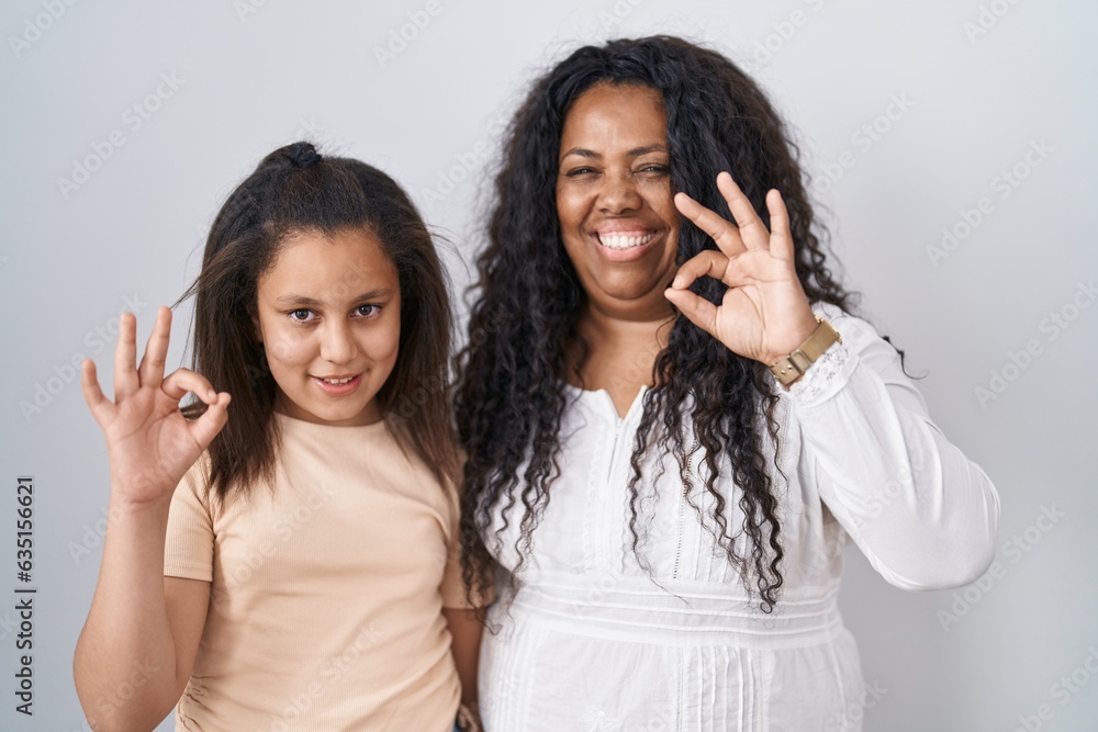 Mother and young daughter standing over white background smiling positive doing ok sign with hand and fingers. successful expression.
