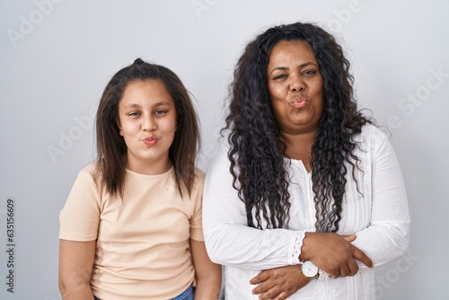 Mother and young daughter standing over white background looking at the camera blowing a kiss on air being lovely and sexy. love expression.