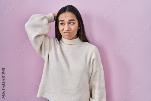 Young south asian woman standing over pink background confuse and wondering about question. uncertain with doubt, thinking with hand on head. pensive concept. © Krakenimages.com