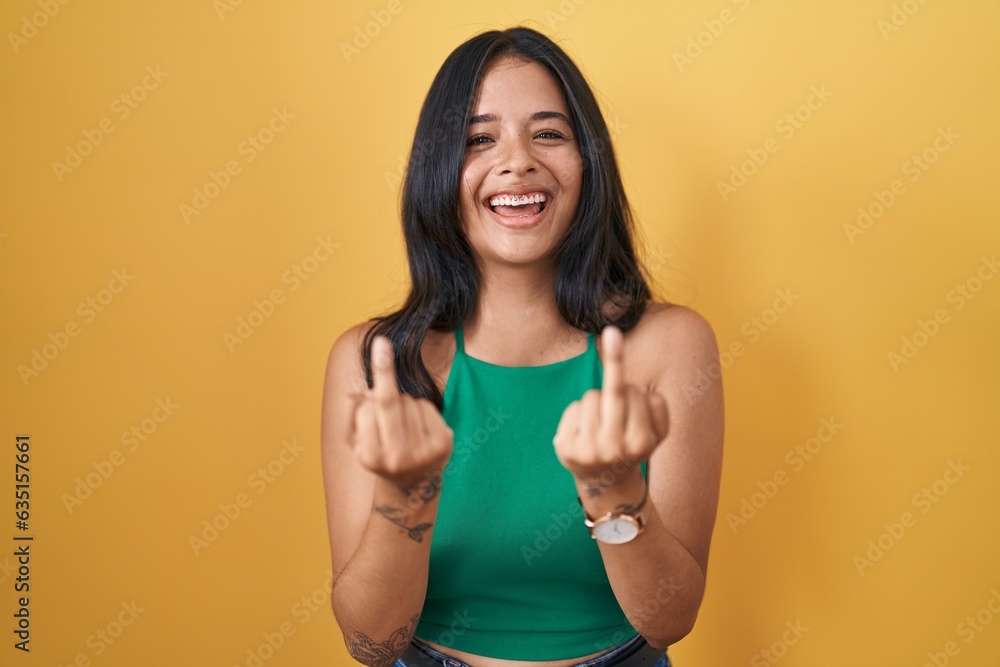Brunette woman standing over yellow background showing middle finger doing fuck you bad expression, provocation and rude attitude. screaming excited Brunette woman standing over yellow background showing middle finger doing fuck you bad expression, provocation and rude attitude. screaming excited