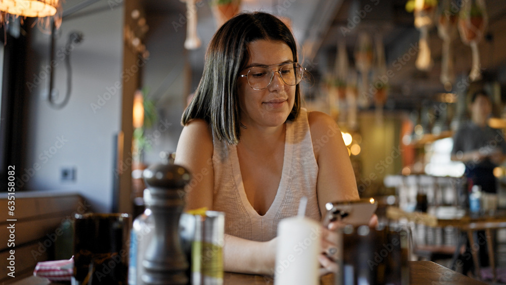 Young beautiful hispanic woman using smartphone sitting on the table at the restaurant