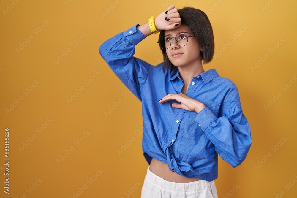 Young girl standing over yellow background touching forehead for illness and fever, flu and cold, virus sick Young girl standing over yellow background touching forehead for illness and fever, flu and cold, virus sick