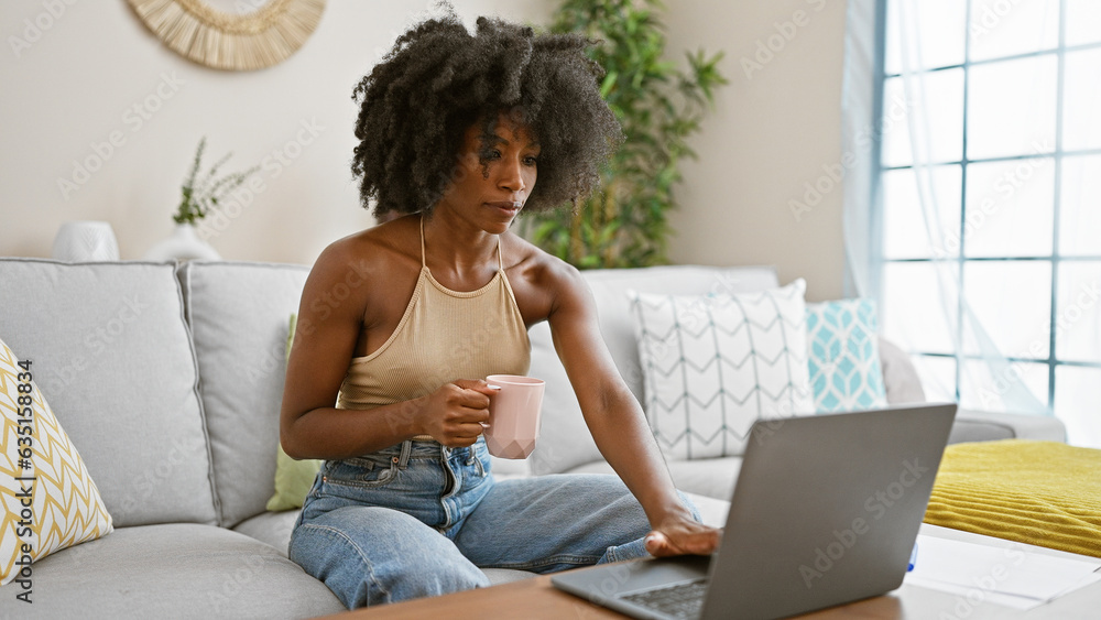 African american woman using laptop drinking coffee at home African american woman using laptop drinking coffee at home