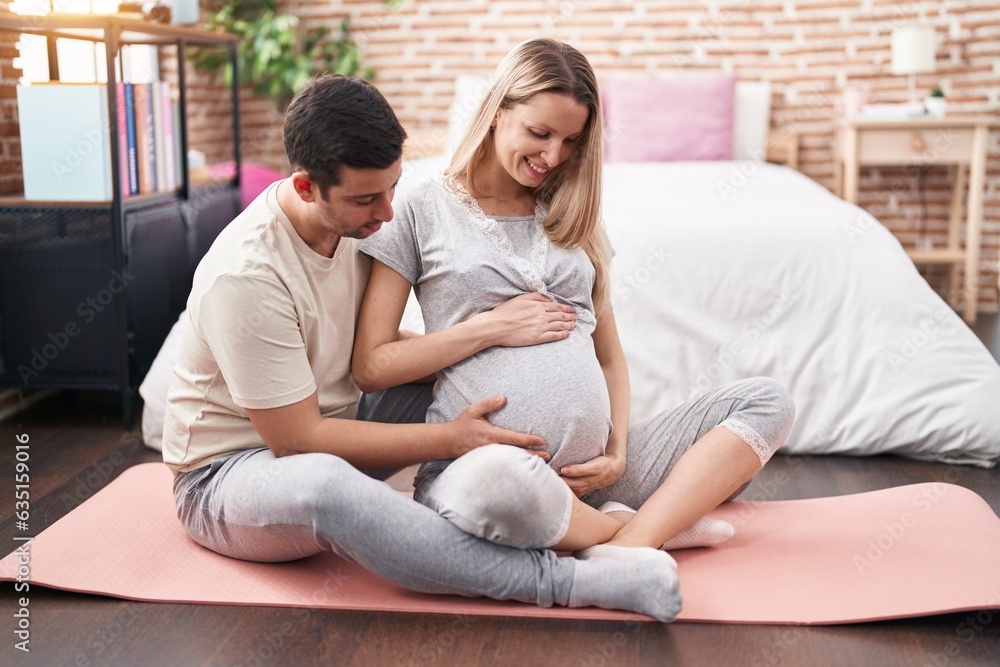 Man and woman couple touching belly sitting on yoga mat at bedroom Man and woman couple touching belly sitting on yoga mat at bedroom
