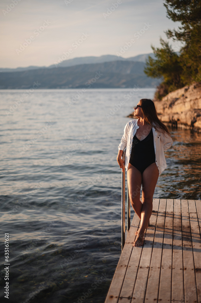 Brunette posing on wooden pier and looking at sunset Brunette posing on wooden pier and looking at sunset
