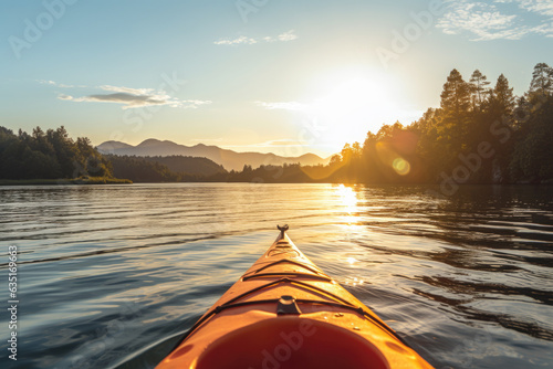 Fototapeta Naklejka Na Ścianę i Meble -  Front of an orange kayak on a lake at sunset. The kayak is pointed towards the horizon and the sun is setting behind the mountains in the background, golden glow