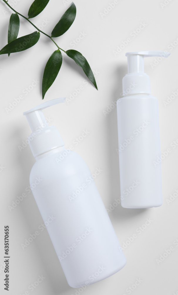 Bottles with different cosmetic products and green leaves on white background, flat lay