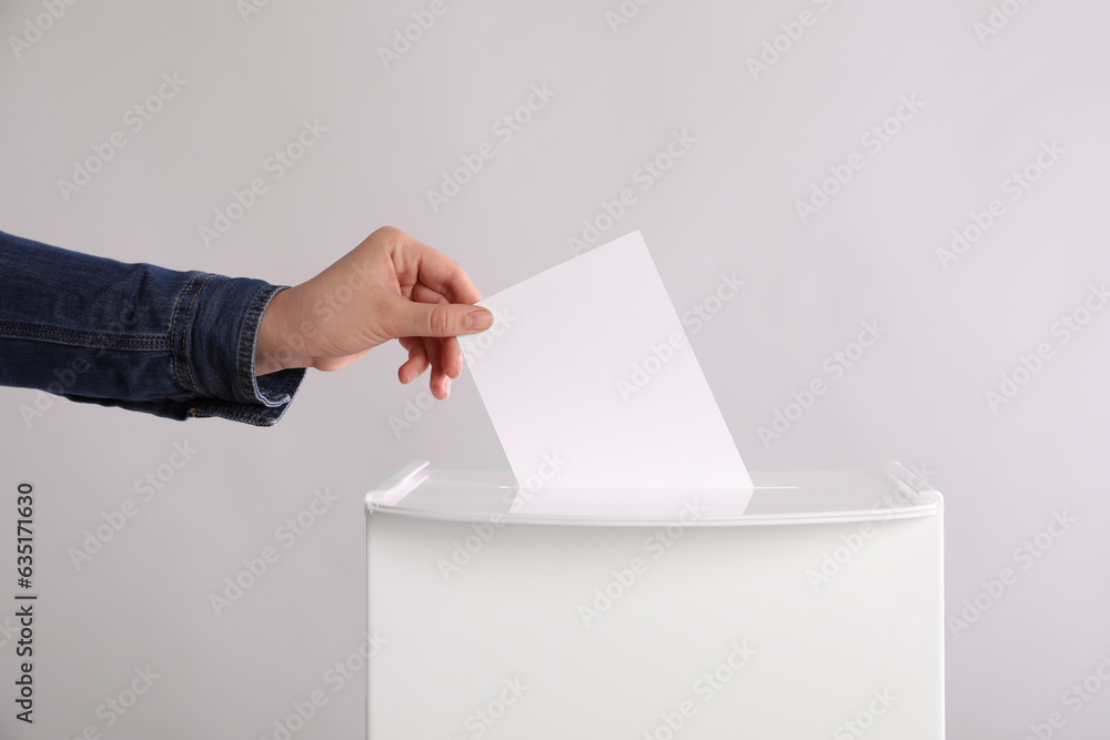 Woman putting her vote into ballot box on light grey background, closeup Woman putting her vote into ballot box on light grey background, closeup
