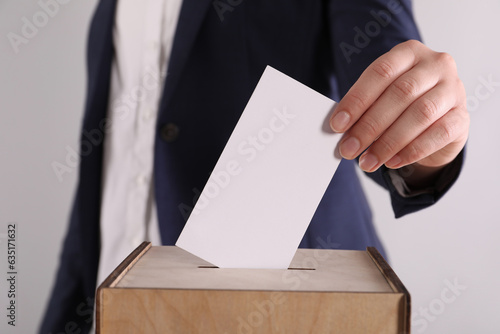 Woman putting her vote into ballot box on light grey background, closeup