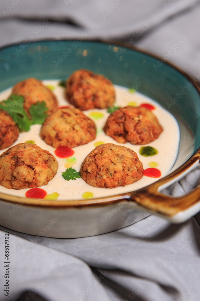 fishballs in white sauce with drops of mint oil and sriracha on a grey steel plate with a grey tablecloth fishballs in white sauce with drops of mint oil and sriracha on a grey steel plate with a grey tablecloth