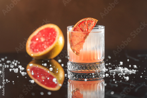 light orange cocktail with a grapefruit slice and coarse sea salt on a mirror table with reflection