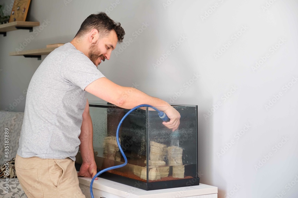 Hispanic man filling up new aquarium with a hose at home. Fishkeeping concept.
