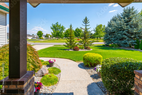 Fototapeta Naklejka Na Ścianę i Meble -  View from the front porch of a modern suburban home with a manicured front lawn in a nice community neighborhood across the street to a park on a sunny summer day.
