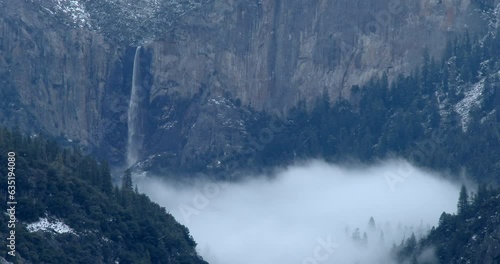 Storm clouds fill Yosemite Valley with Bridal Veil Falls flowing into canyon in winter