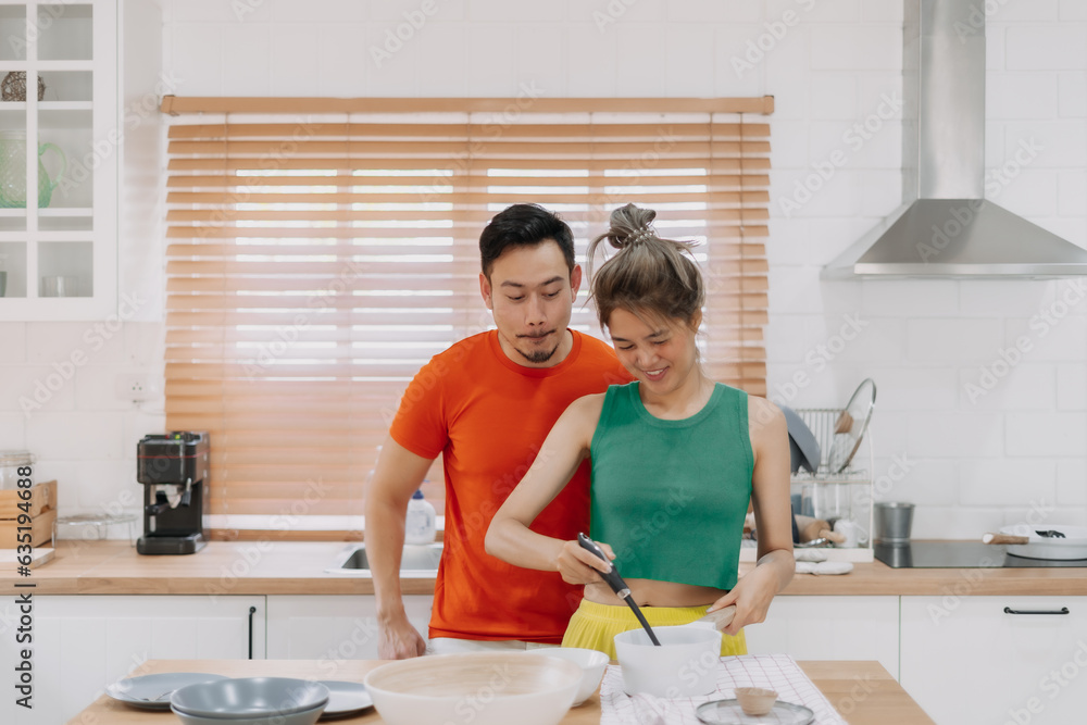 Husband looking at wife who cooking lunch for him. Happy asian couple in kitchen Husband looking at wife who cooking lunch for him. Happy asian couple in kitchen
