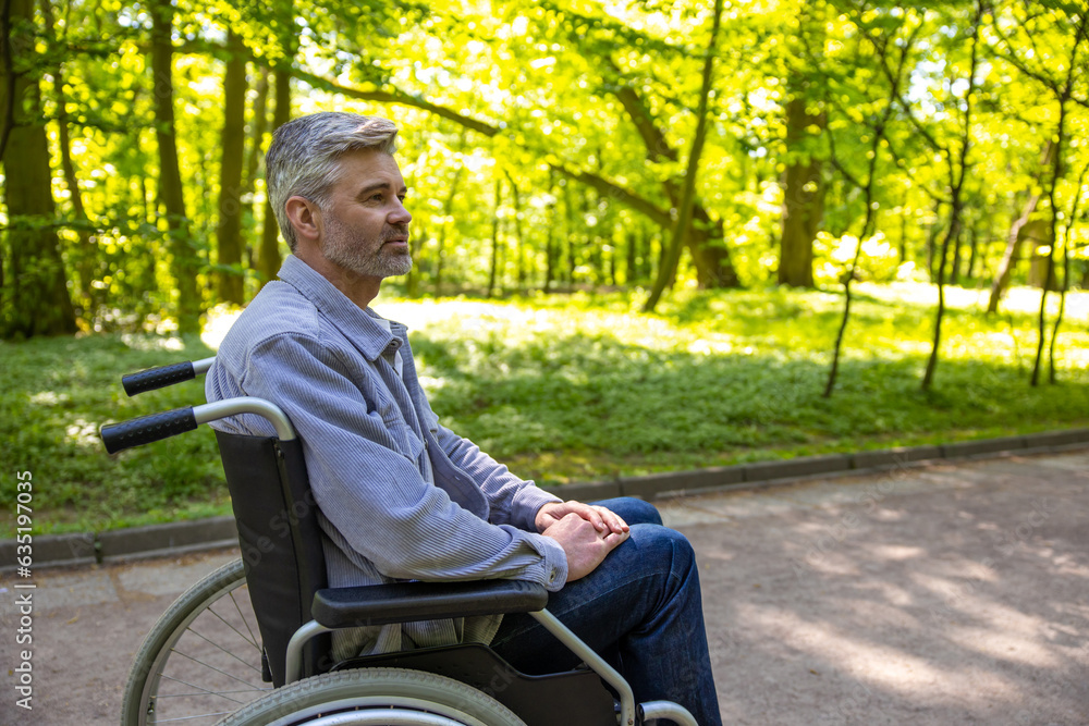 Disable man wearing casual clothing spending time in summer park riding wheelchair. Disable man wearing casual clothing spending time in summer park riding wheelchair.