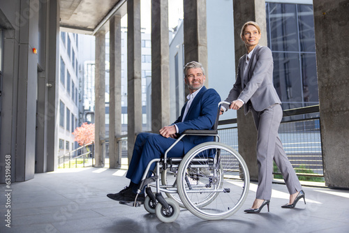 Woman assisting man business partner in wheelchair going to office. © zinkevych