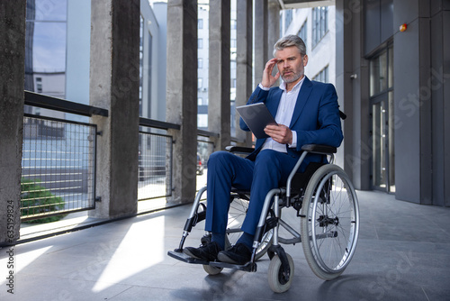Pensive business man in wheelchair with tablet using mobile device for work outdoors.