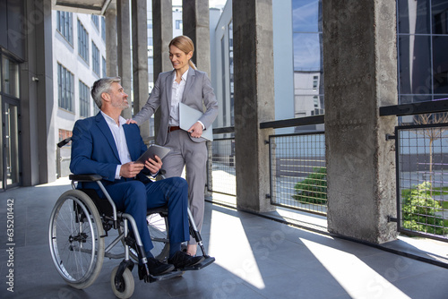 Business partners with adult gray haired man in wheelchair talking outdoors. © zinkevych