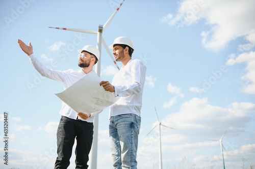 Two engineers discussing against turbines on wind turbine farm. photo