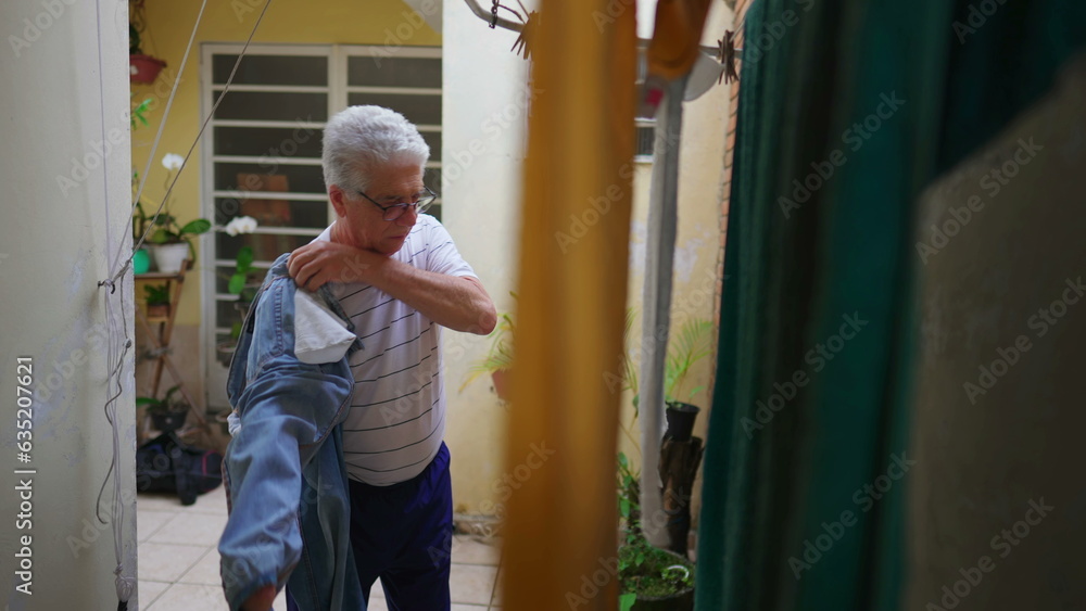 Senior man reverting pants from the inside out after drying on hanger, older person doing domestic chore routine by straightening jeans