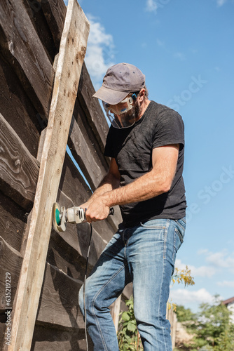 Man work on holiday repairing and renovating a country house - summer chores in the backyard and garden - power tool work