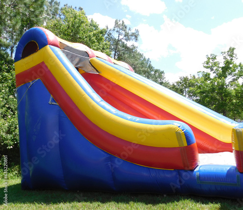 Red, yellow, and blue bounce house slide outside on a bright and sunny summer day.
