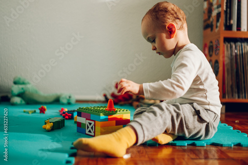 Side view of a cute little boy entertaining himself and playing a fun game with plastic bricks at home.