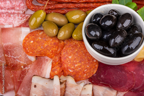 Full frame of appetizers of olives and cuts of sausages, bacon and prosciutto.