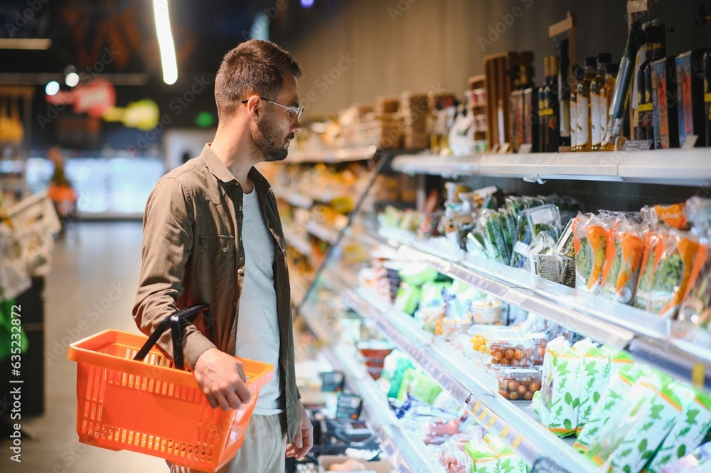 Handsome man buying some healthy food and drink in modern supermarket or grocery store. Lifestyle and consumerism concept