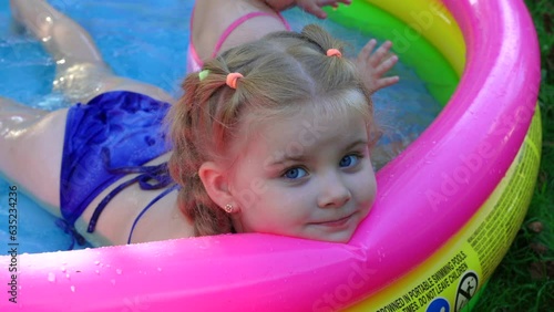Children in the pool, it's hot in the summer. A little girl. A child plays in a children's pool. Swimming in the yard, inflatable pool in the shade. The girl loves water. Happy child in a swimsuit