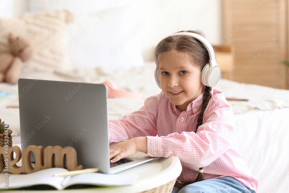 Little girl in headphones with laptop studying computer sciences online at home Little girl in headphones with laptop studying computer sciences online at home