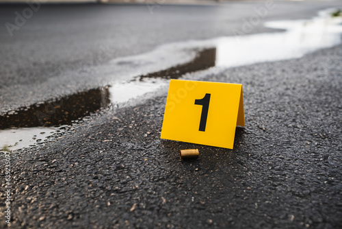 Fotografiet One yellow crime scene evidence marker on the street after a gun shooting brass