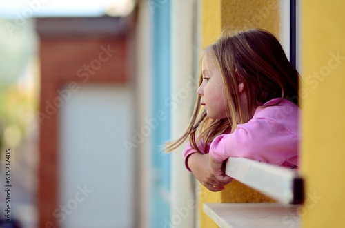 Photos Selective focus of little girl looking out window at second floor home in warm a